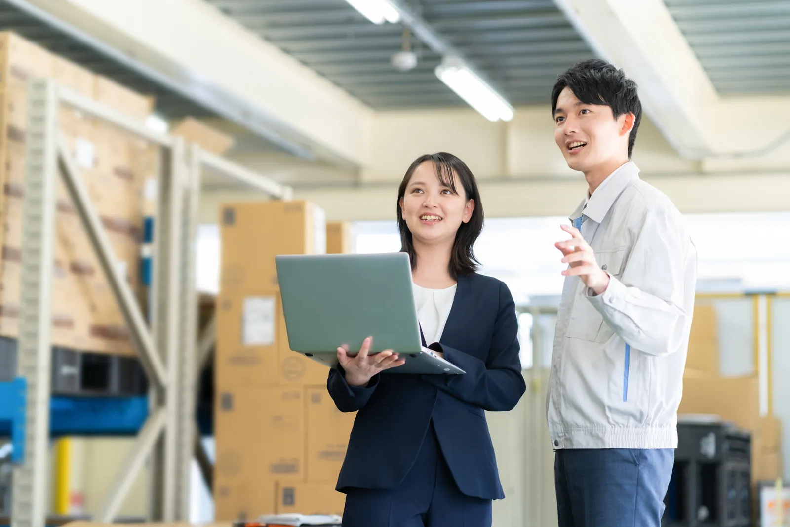 倉庫でノートパソコンを確認しながら相談する二人の担当者