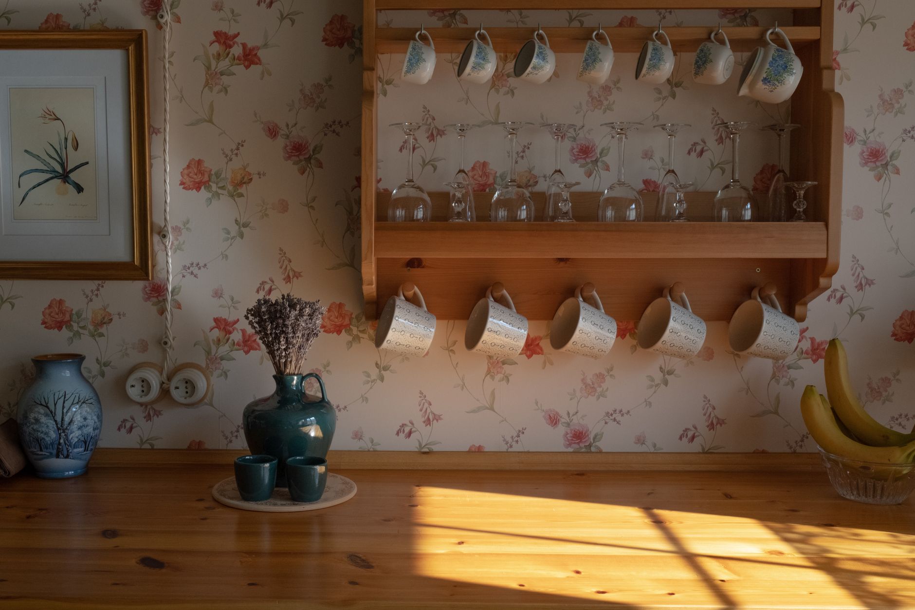 Vintage kitchen scene with floral mugs on a wooden shelf, su