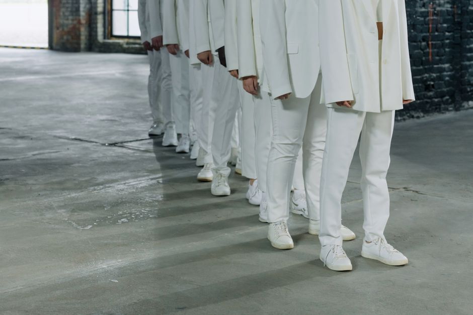 A row of individuals dressed in white suits and sneakers sta