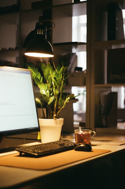 A warm-lit desk with a computer, lamp, plant, and tea cup in