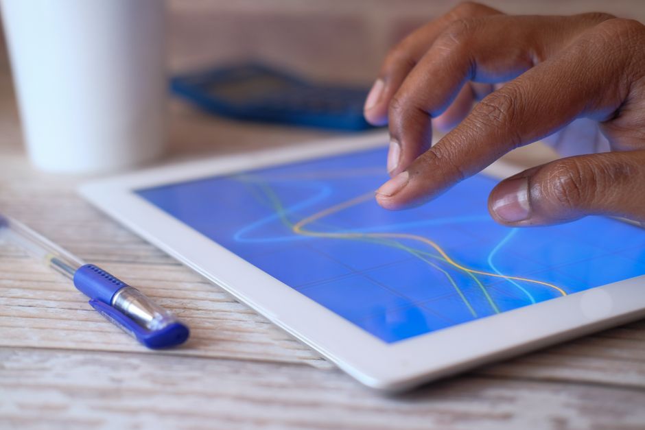 A hand interacting with a digital tablet on a wooden table,