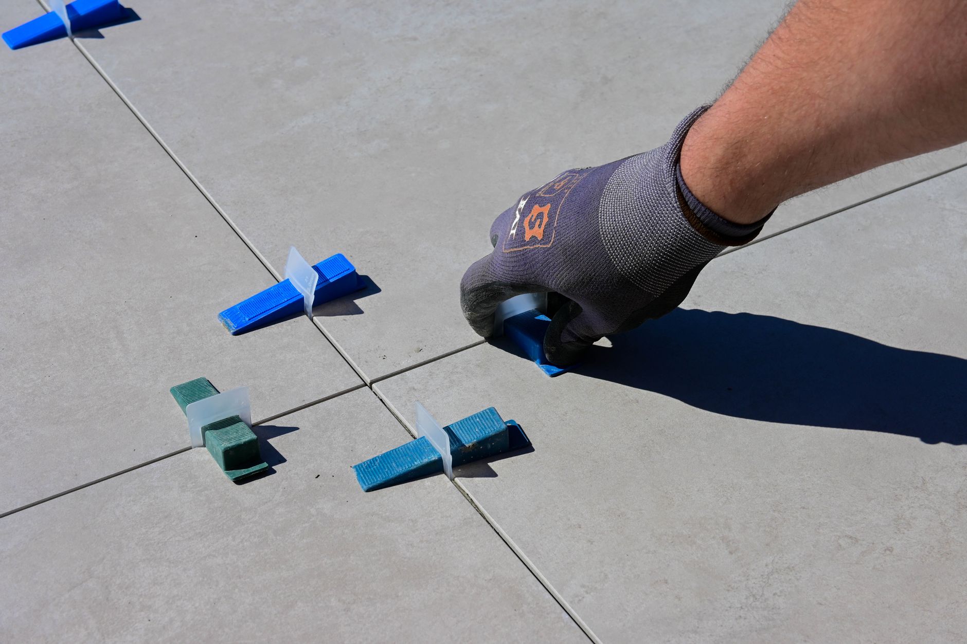 A close-up of a gloved hand installing tiles with spacers on