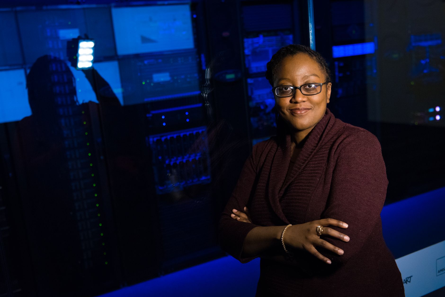 Professional woman standing confidently in a data center, surrounded by glowing servers.