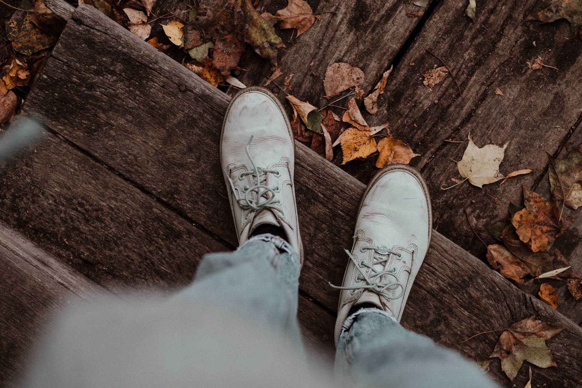 White shoes standing on wooden steps surrounded by autumn le
