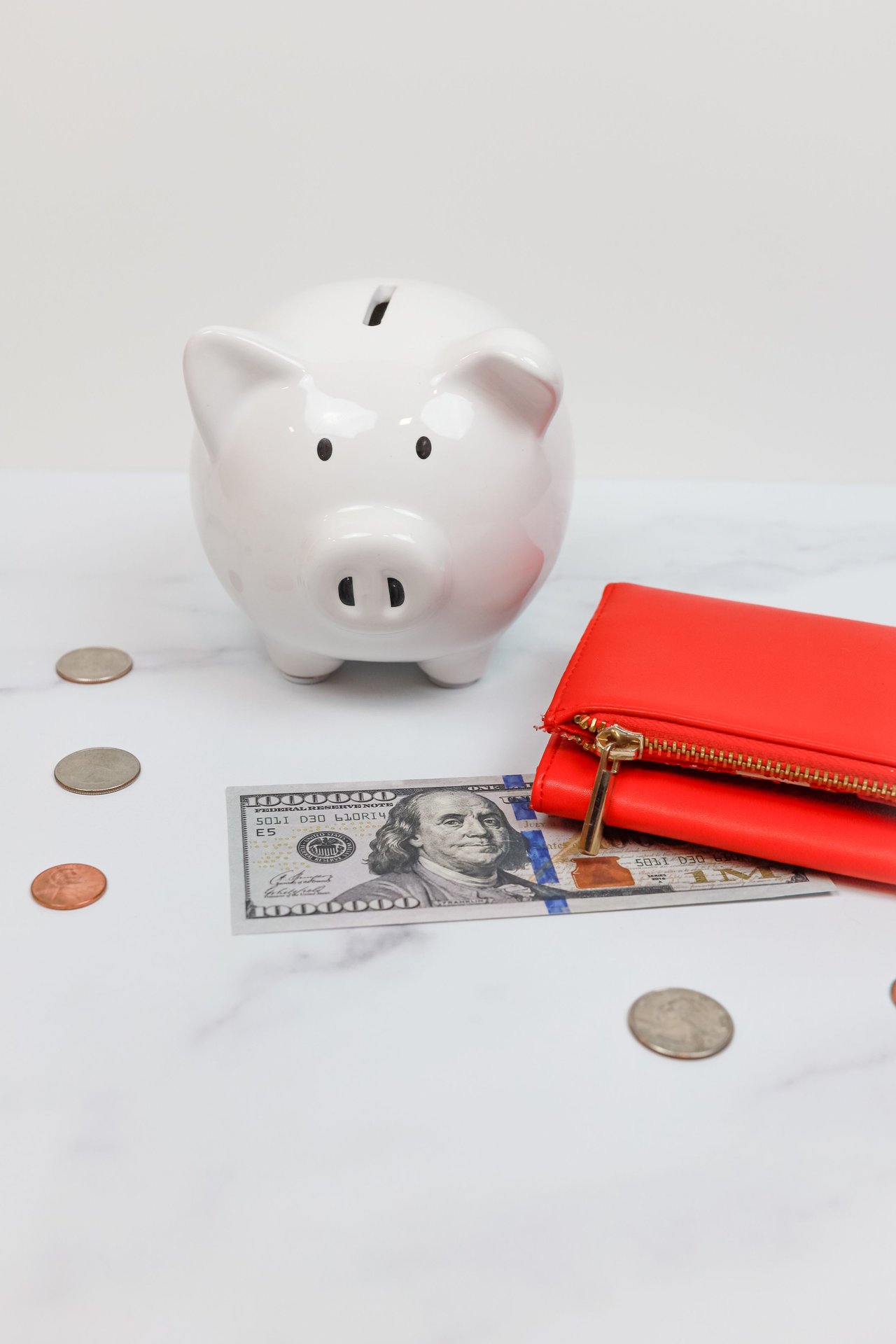 White piggy bank with coins and a red wallet on a marble des