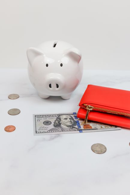 White piggy bank with coins and a red wallet on a marble des