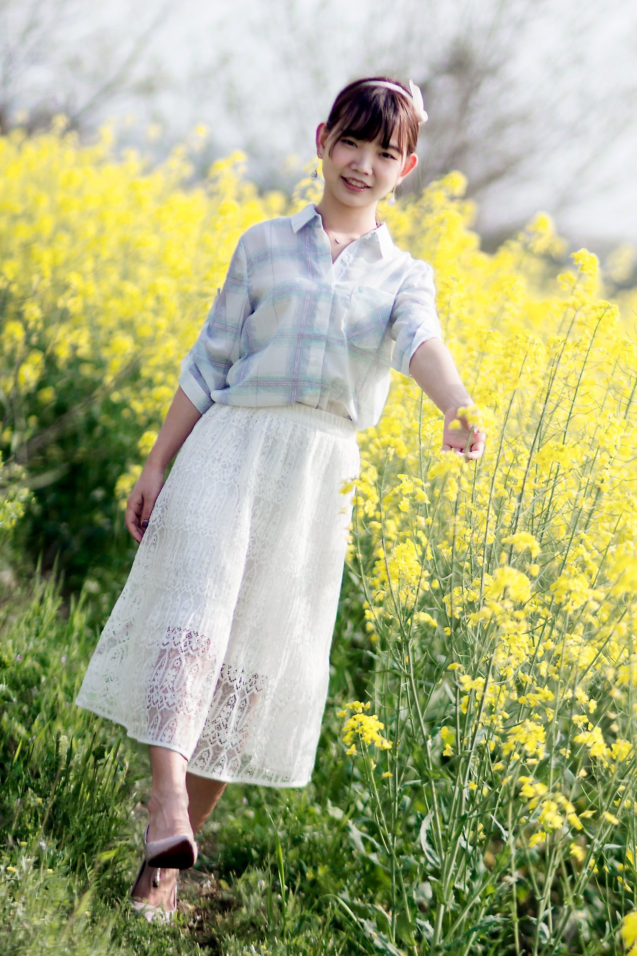 Young girl joyfully posing in a vibrant yellow flower field under daylight.