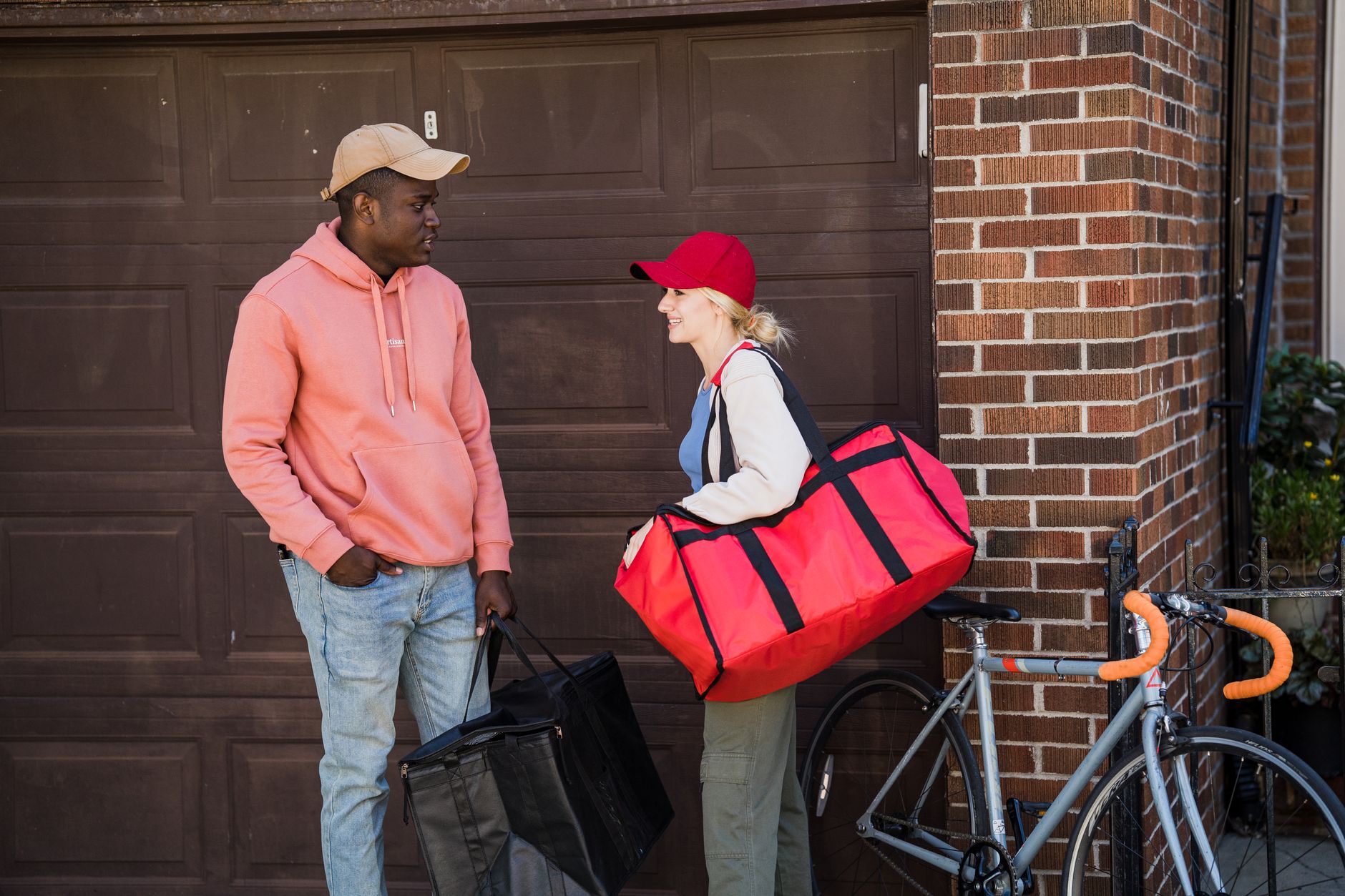 Two delivery workers chat outside a garage, each carrying ba