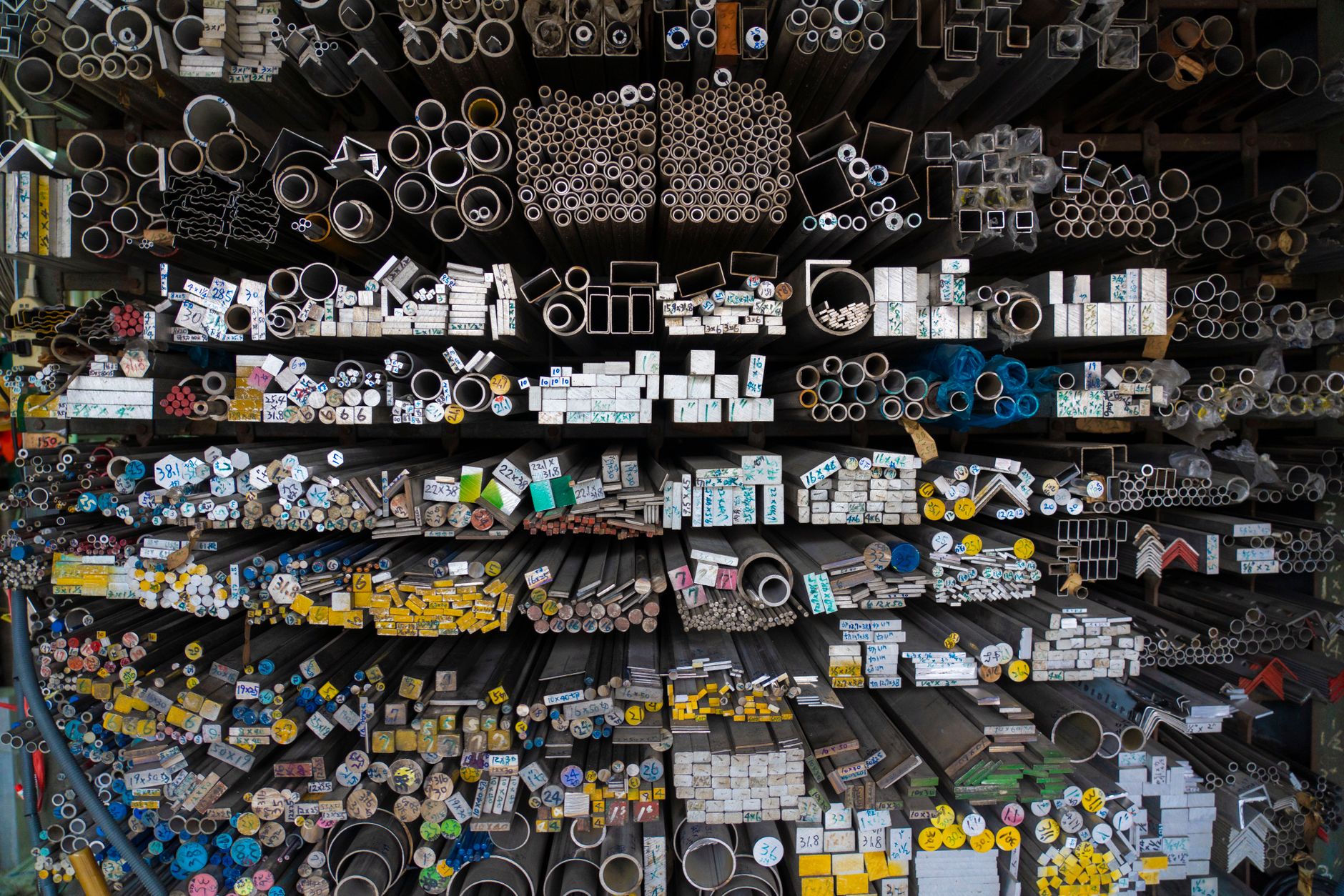 Diverse collection of stacked metallic pipes and rods in a warehouse display.