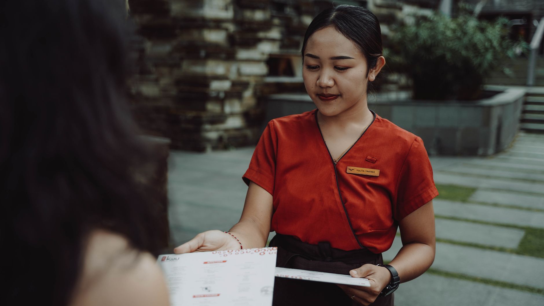 A waitress in a red uniform handing a menu to a guest at an