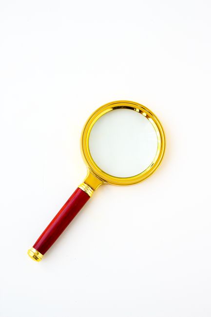 A luxury magnifying glass with a gold frame and red handle o