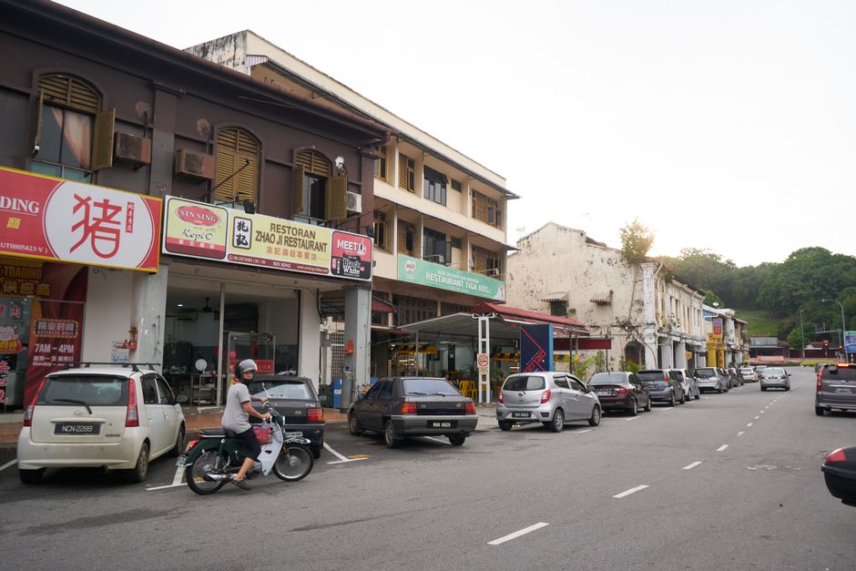 A lively city street with parked cars, motorbike, and shops