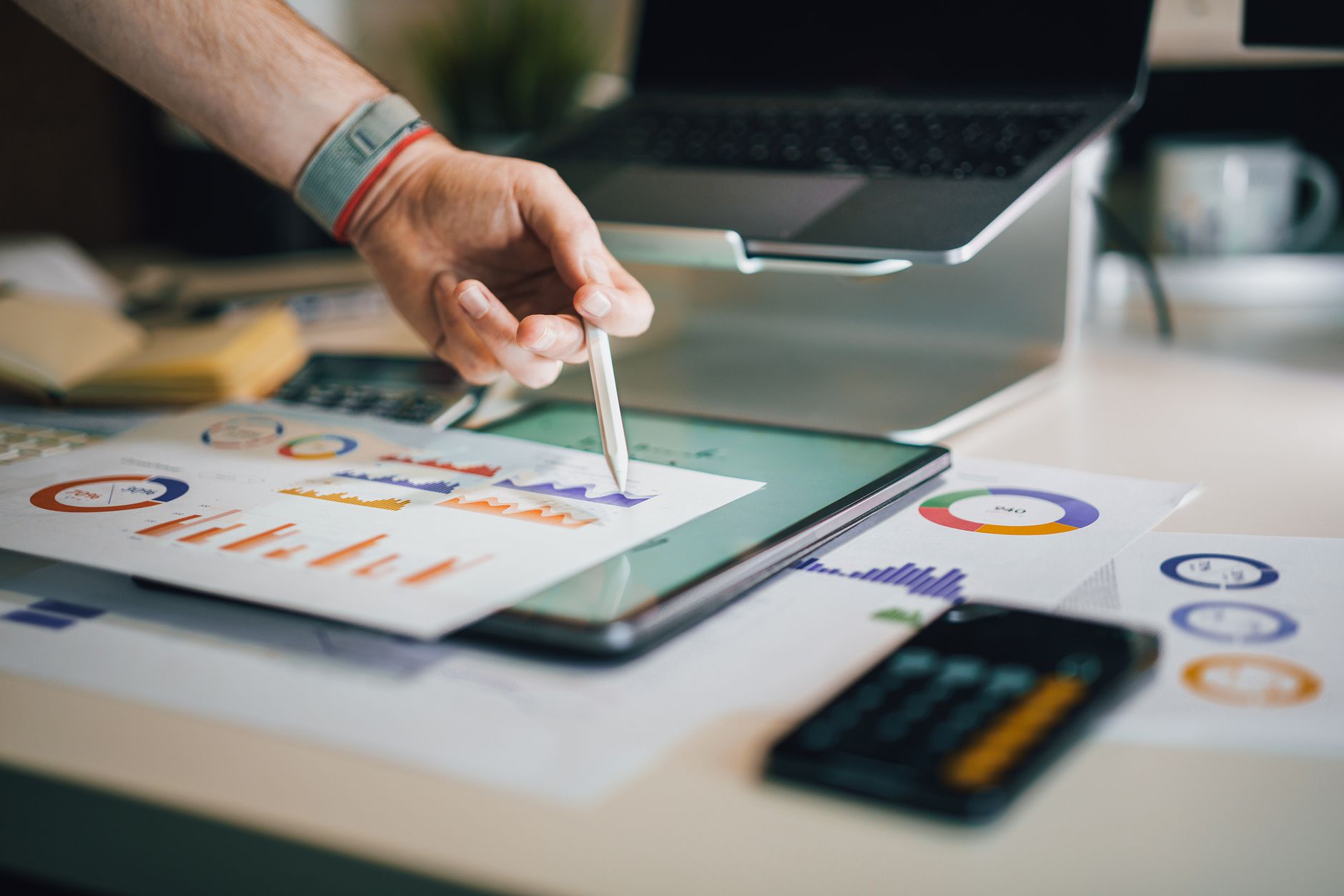 Hand using a tablet and charts on desk to analyze business d