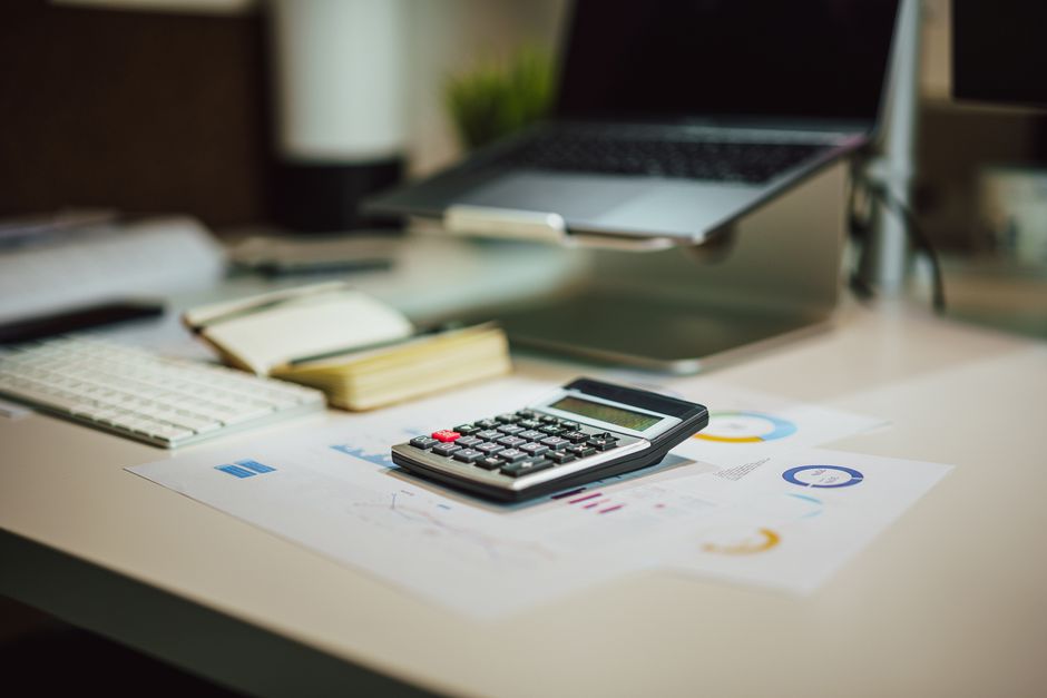 A modern workspace with a laptop, calculator, and documents