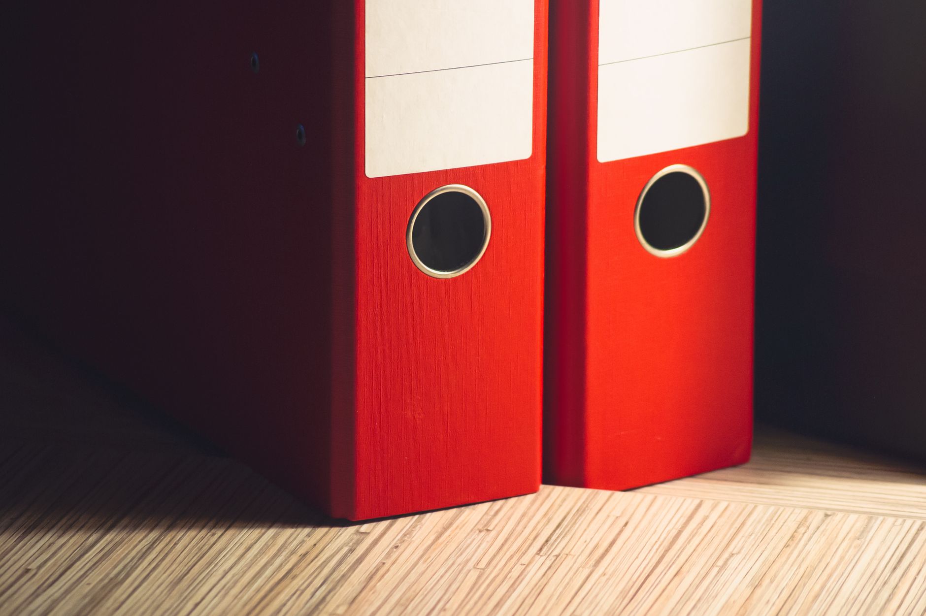 Close-up of two red lever arch files on a wooden desk in a m