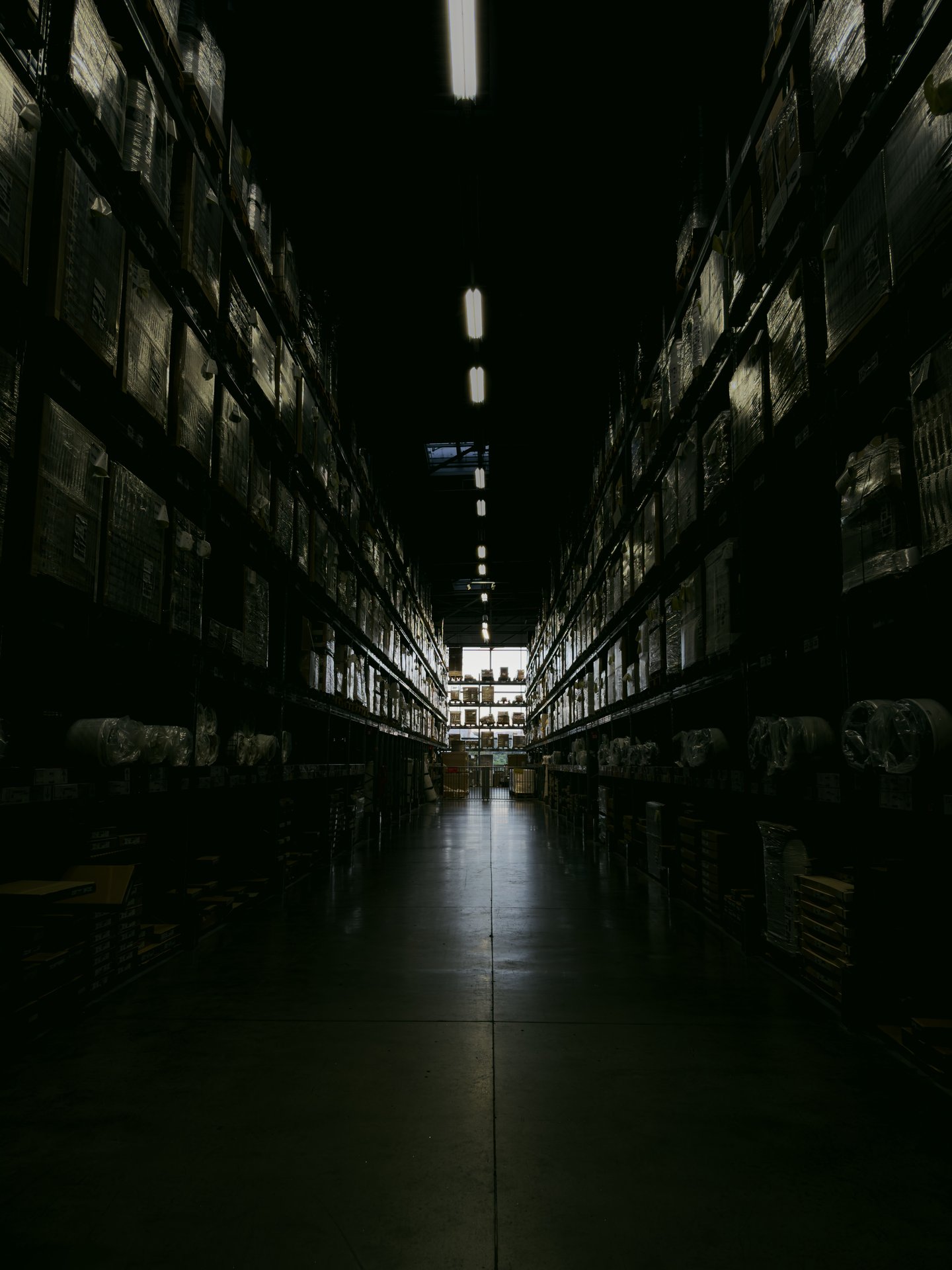 A dark, narrow warehouse aisle with shelves filled with boxe