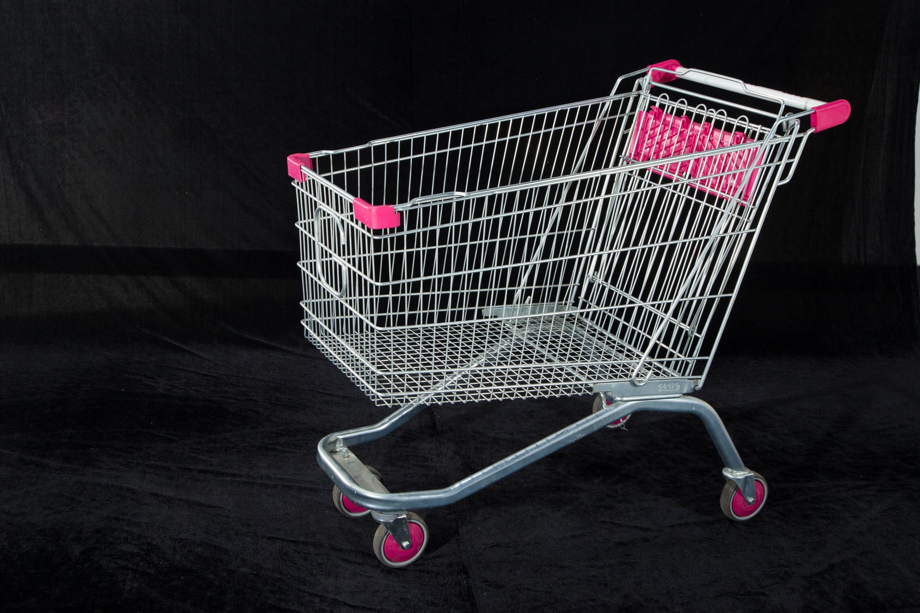 A metal shopping cart with pink handles and wheels on a dark