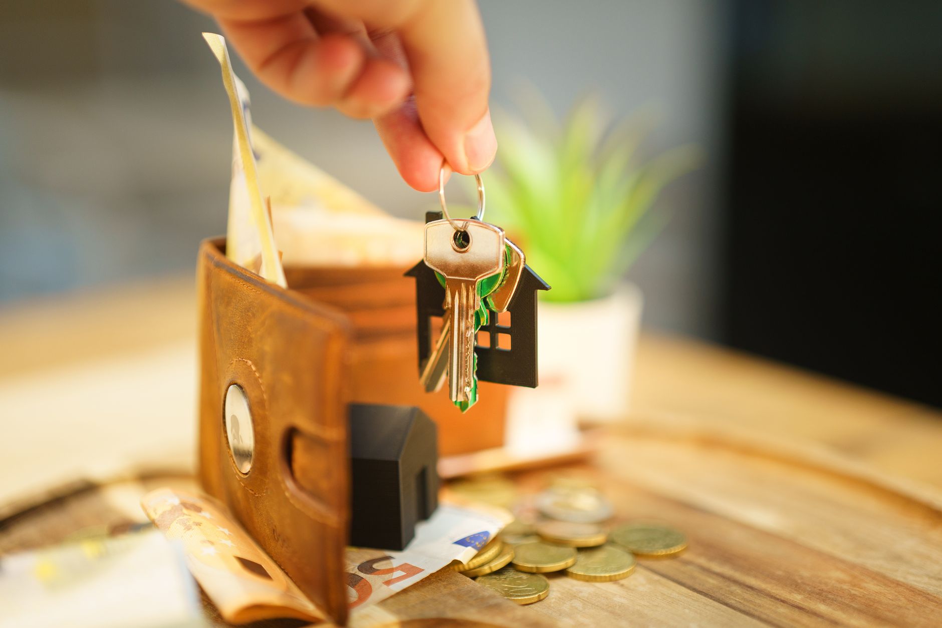 Close-up of hand holding a house key with a wallet and coins