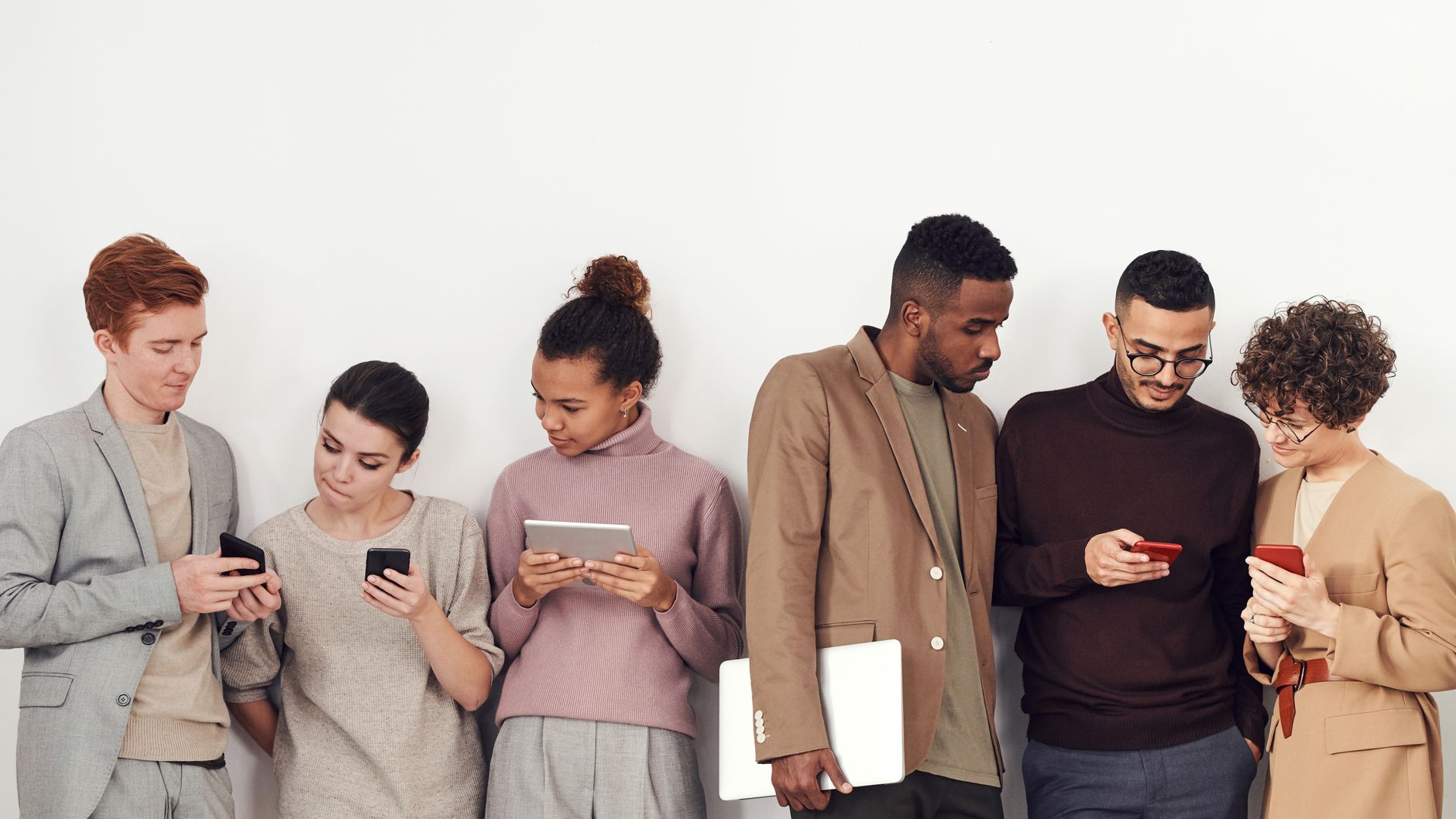Five adults in casual wear using phones and tablets indoors,