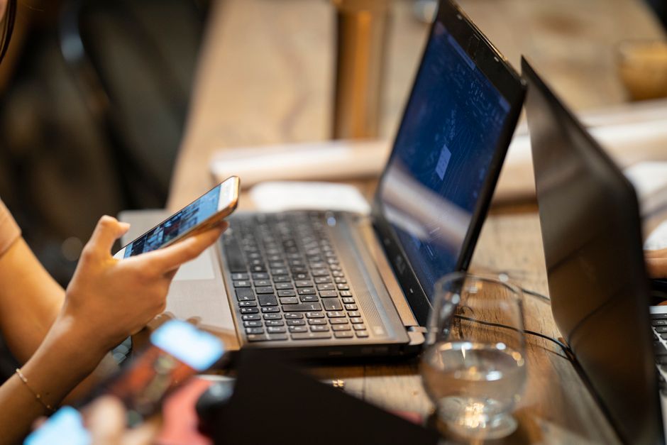 Person using smartphone and laptop in a cozy indoor workspace setting.