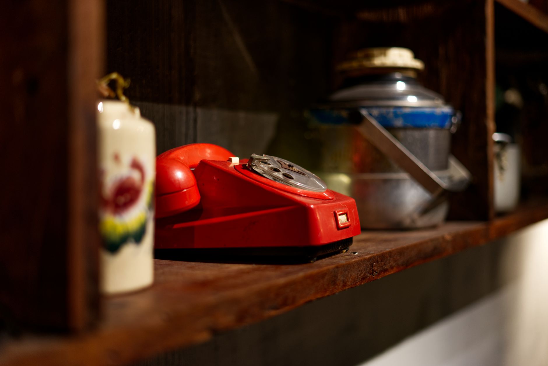 A vintage red rotary telephone sits on a rustic wooden shelf