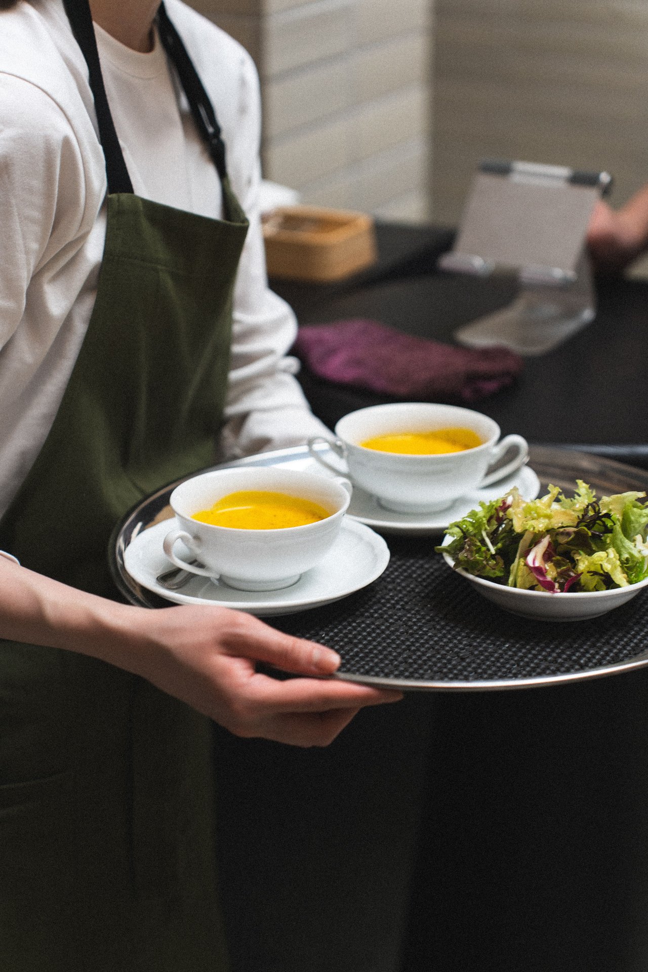 A waiter serving pumpkin soup and salad on a tray in a moder