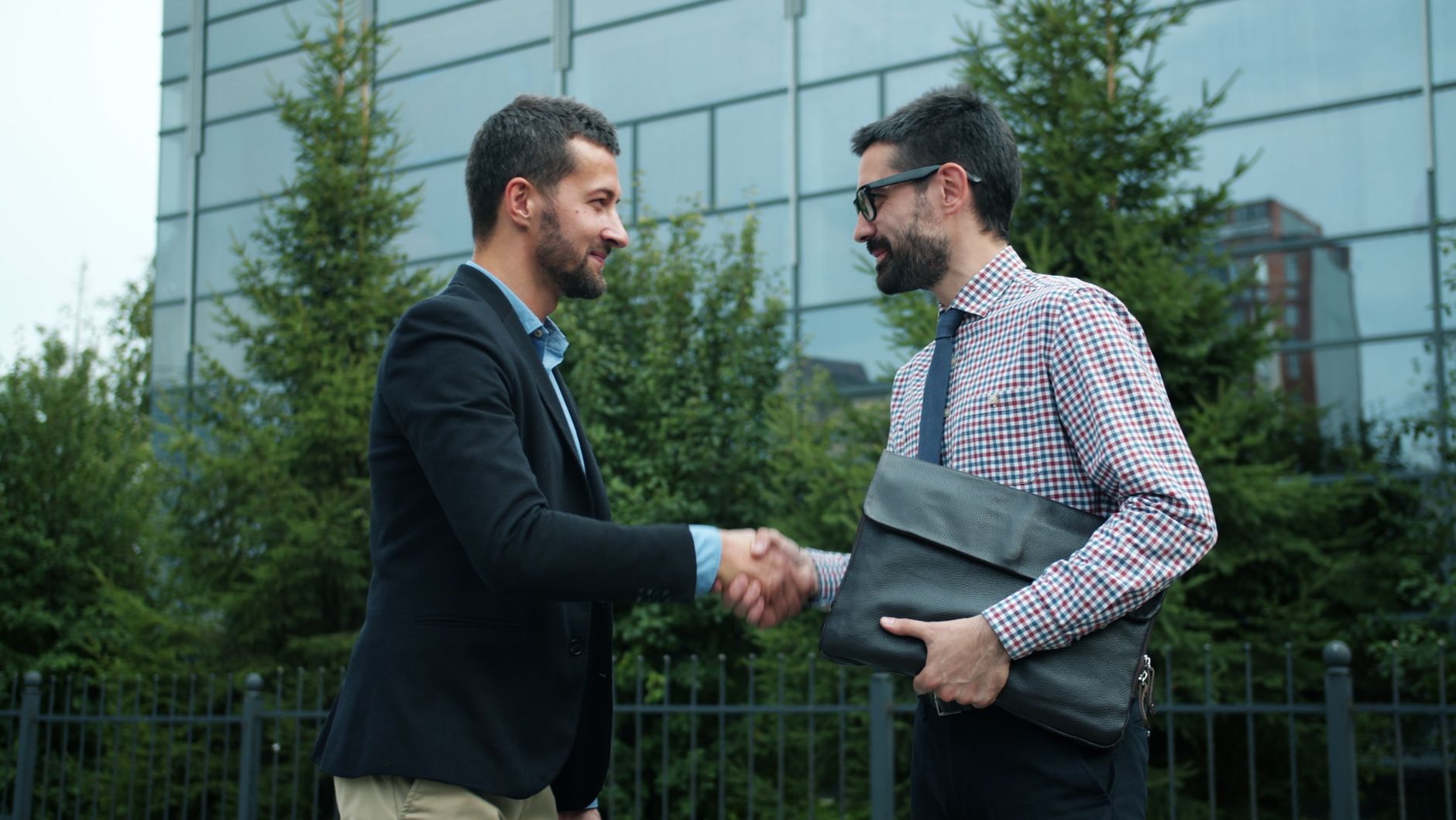 Two businessmen shaking hands outside a modern office buildi
