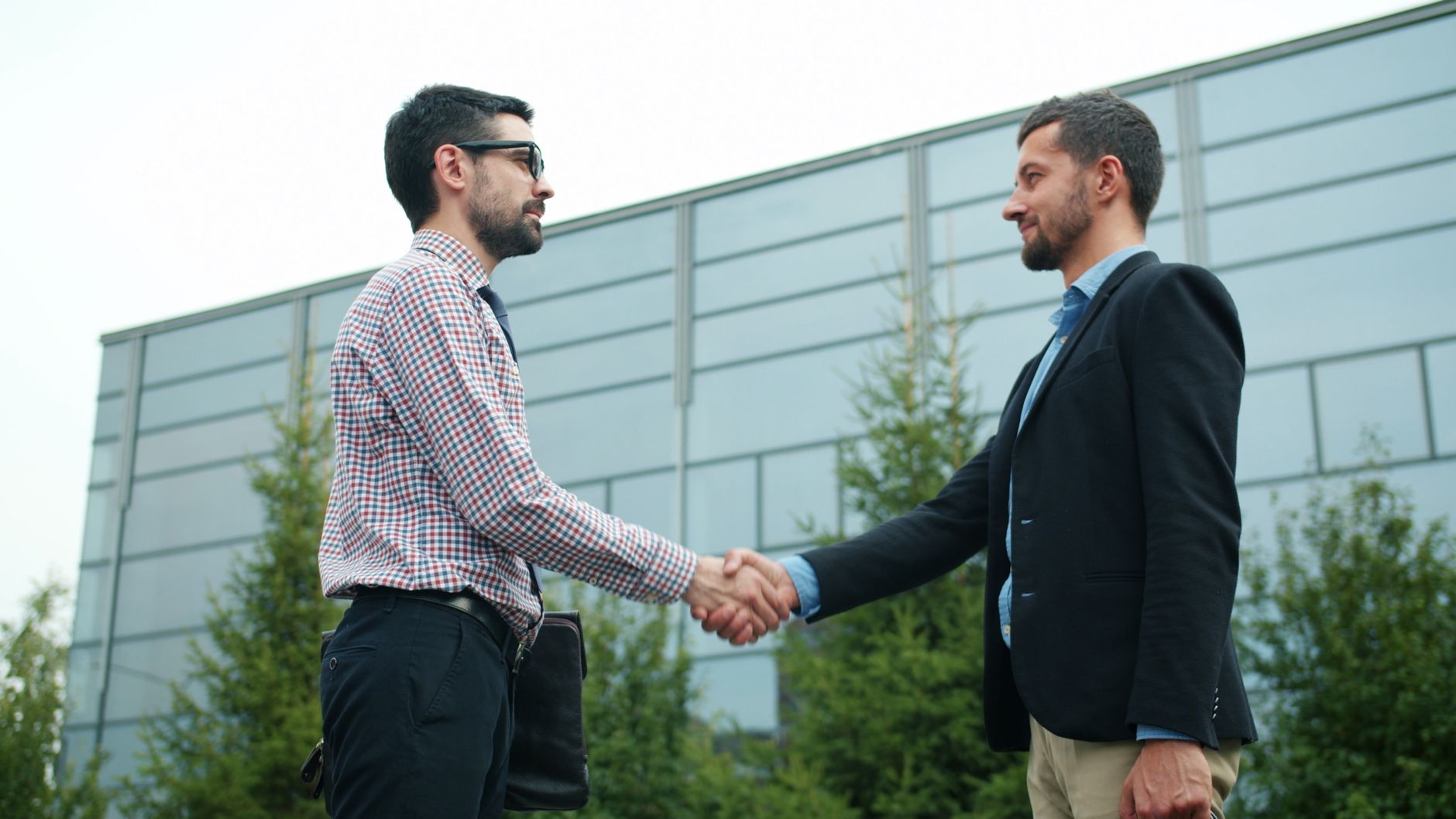 Two businessmen in casual attire shaking hands outside a mod