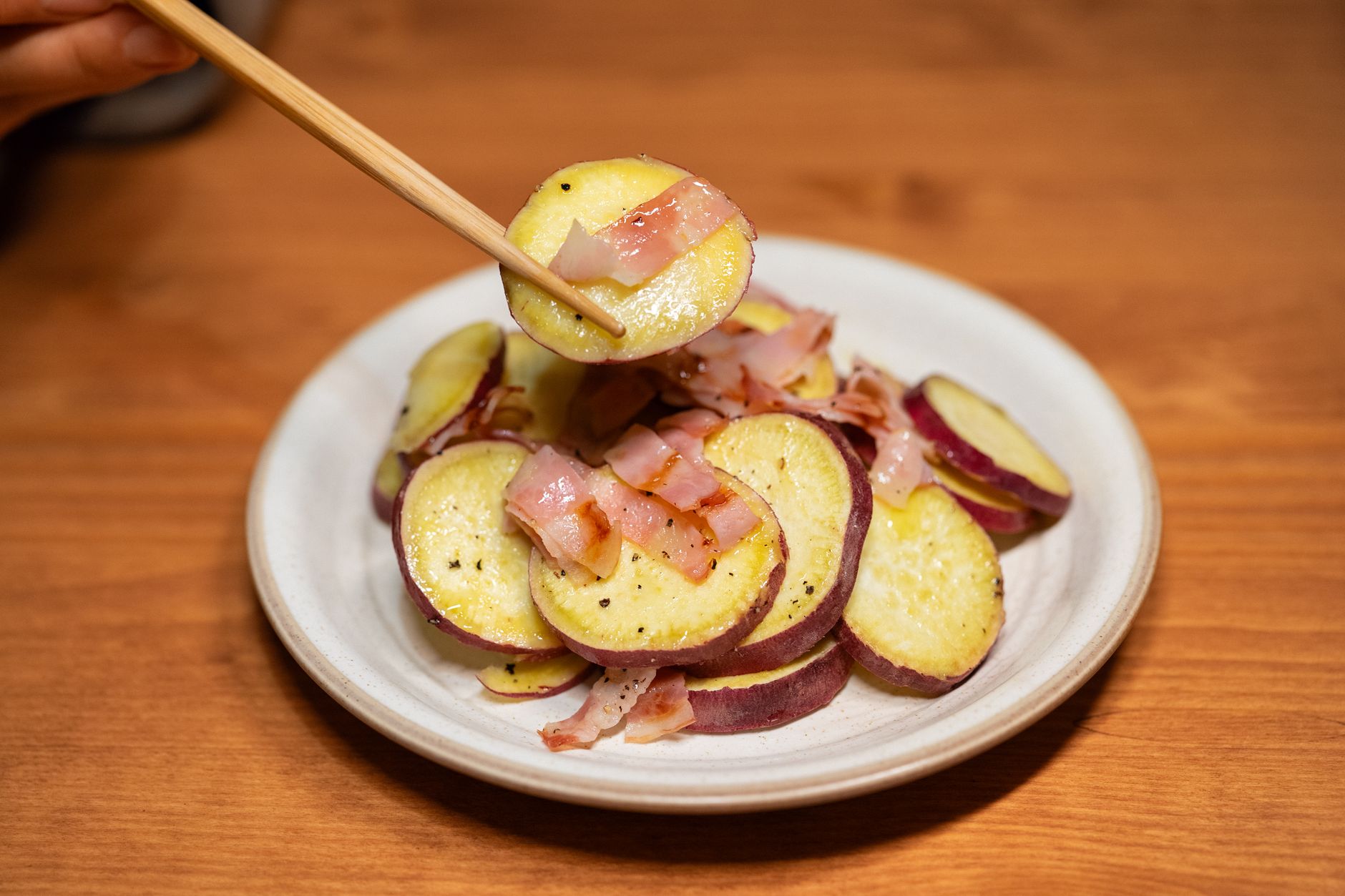Sliced sweet potatoes with bacon served on a white plate, pe