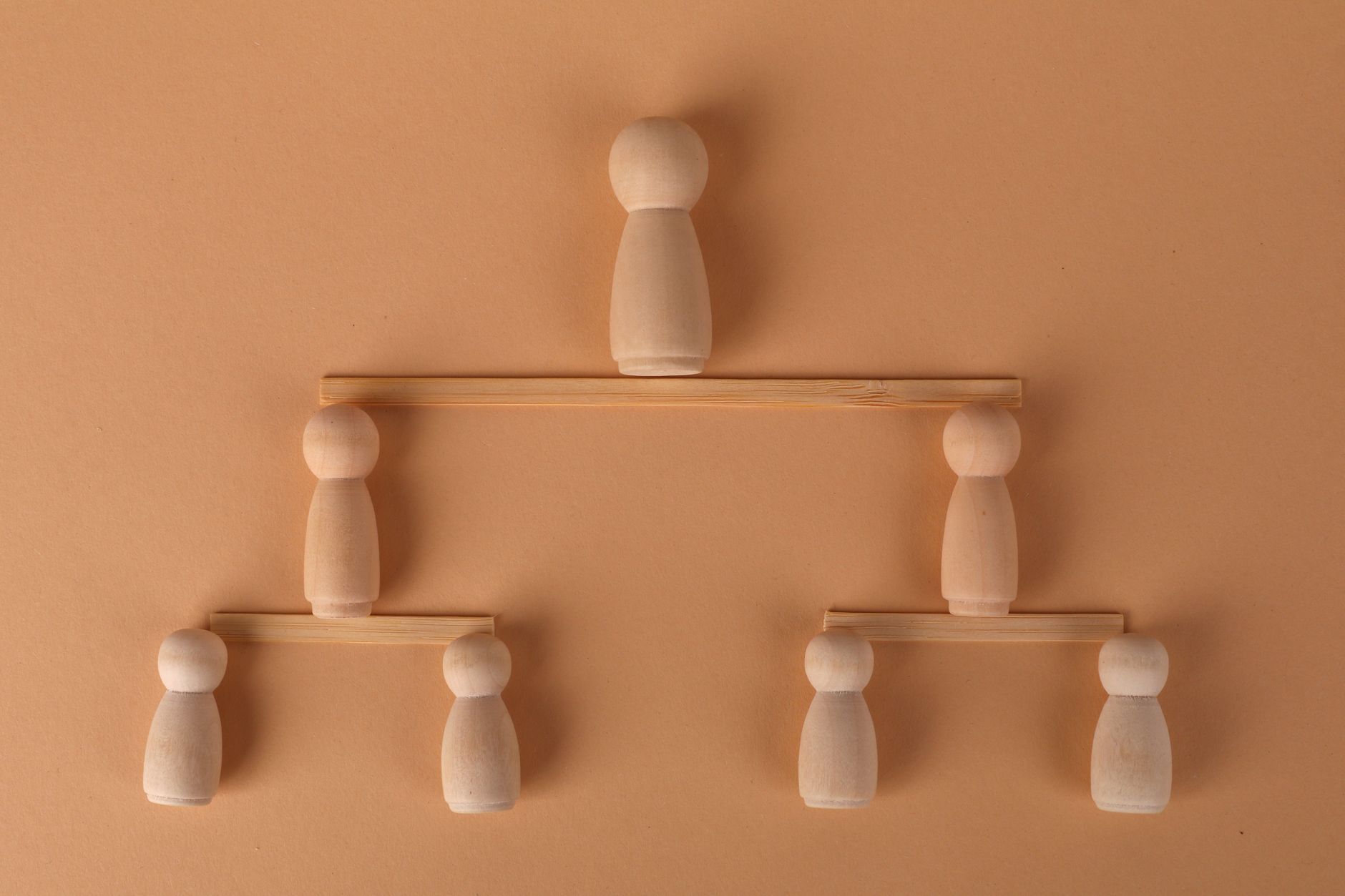 Wooden peg dolls arranged to symbolize a hierarchy on a neut