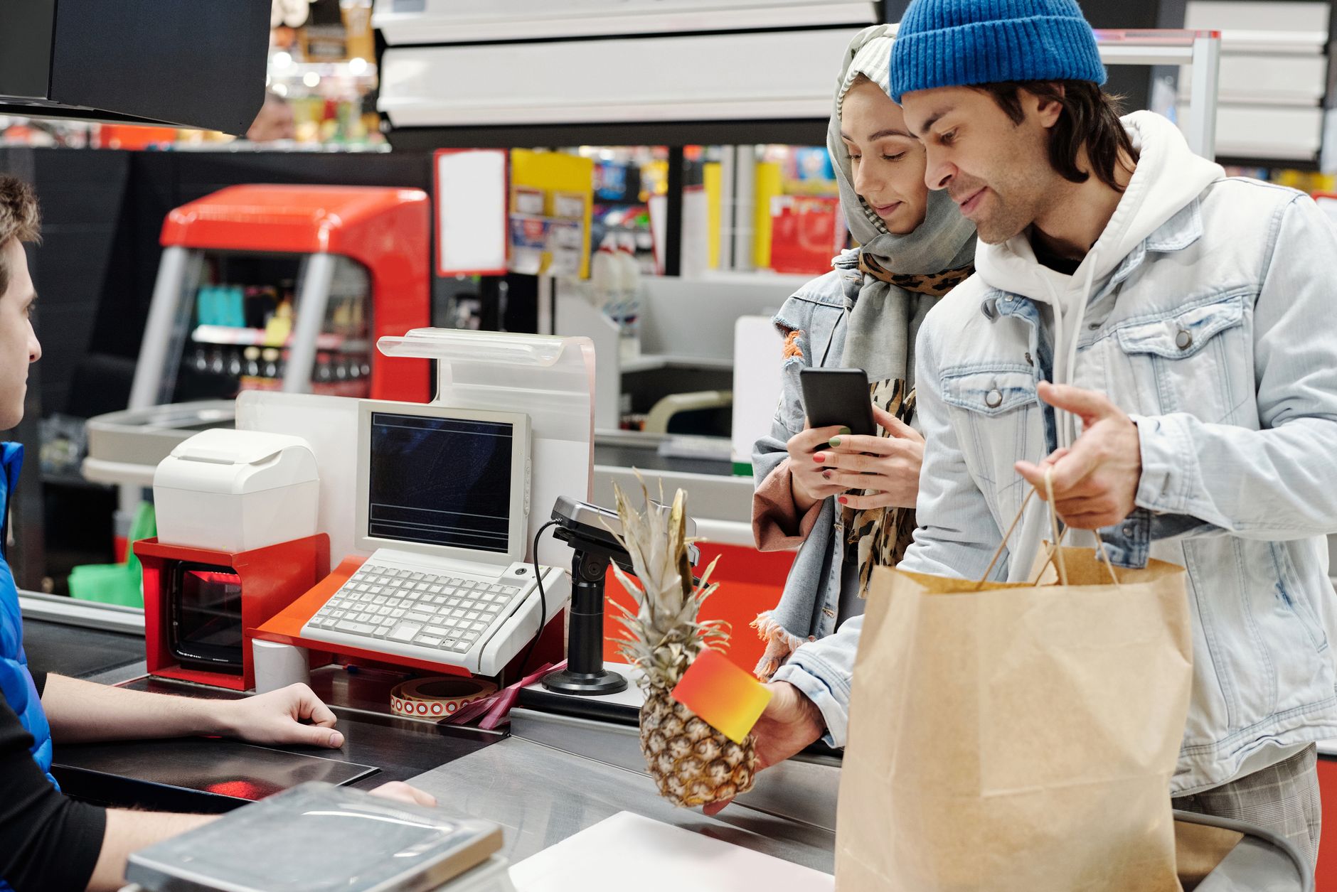 A couple shopping at a supermarket checkout, holding a pinea