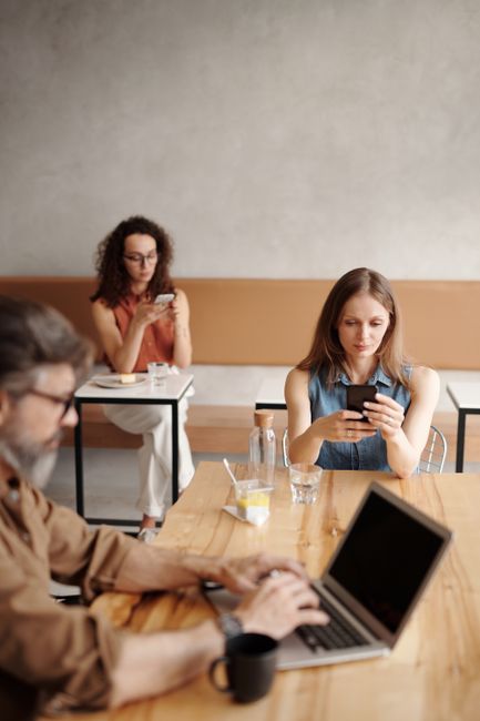 Adults engaging with phones and laptop in a modern coffee sh