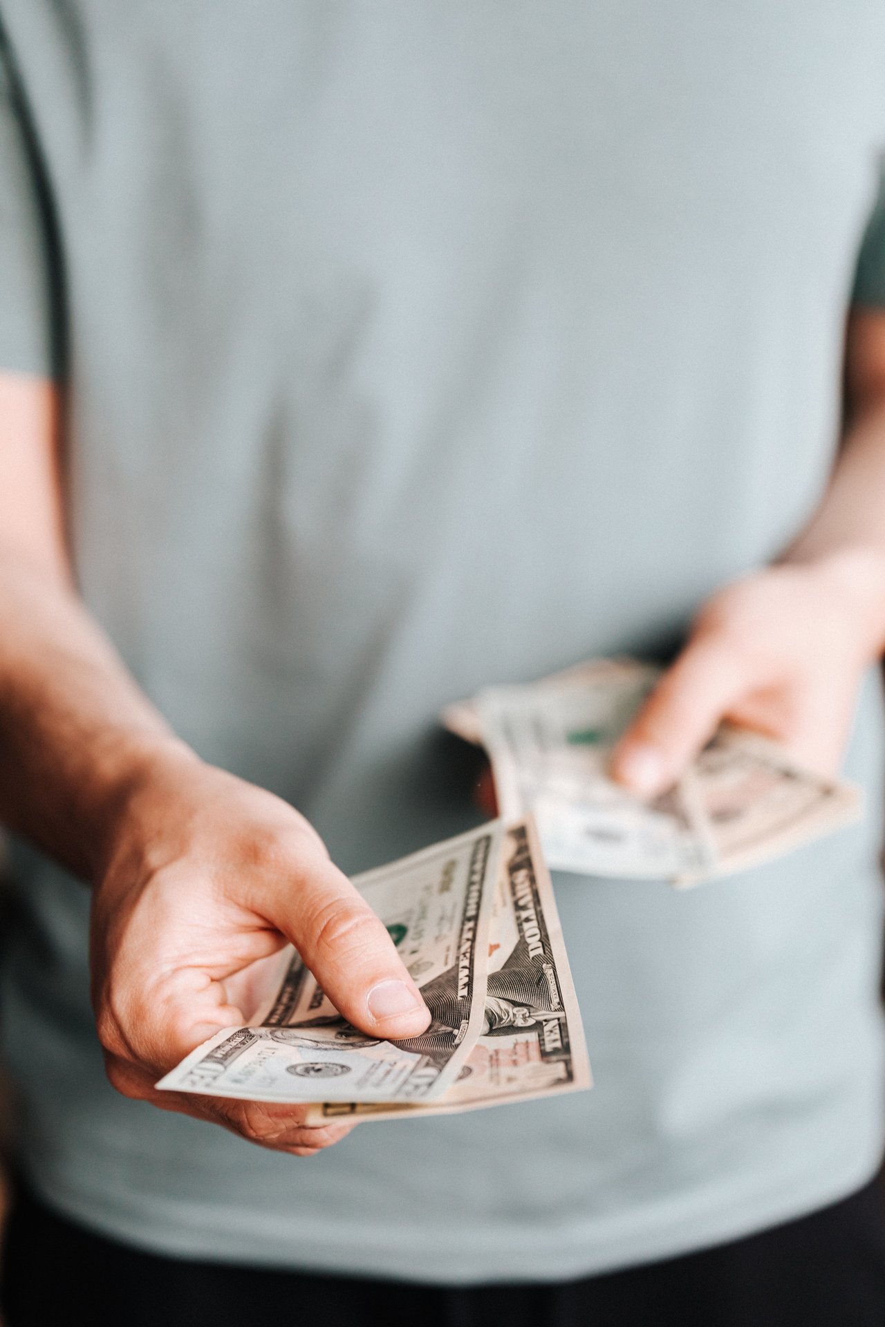 Unrecognizable male in casual clothes holding cash and paying with paper banknotes