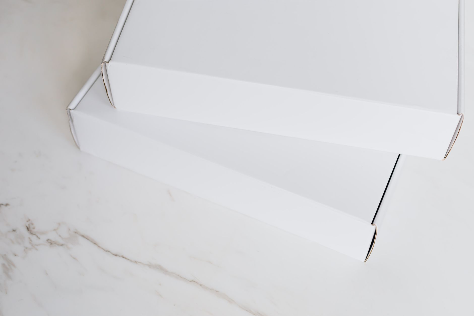 From above of pair of closed white cardboard boxes for postal or courier delivery arranged on white marble tabletop for sending preparation