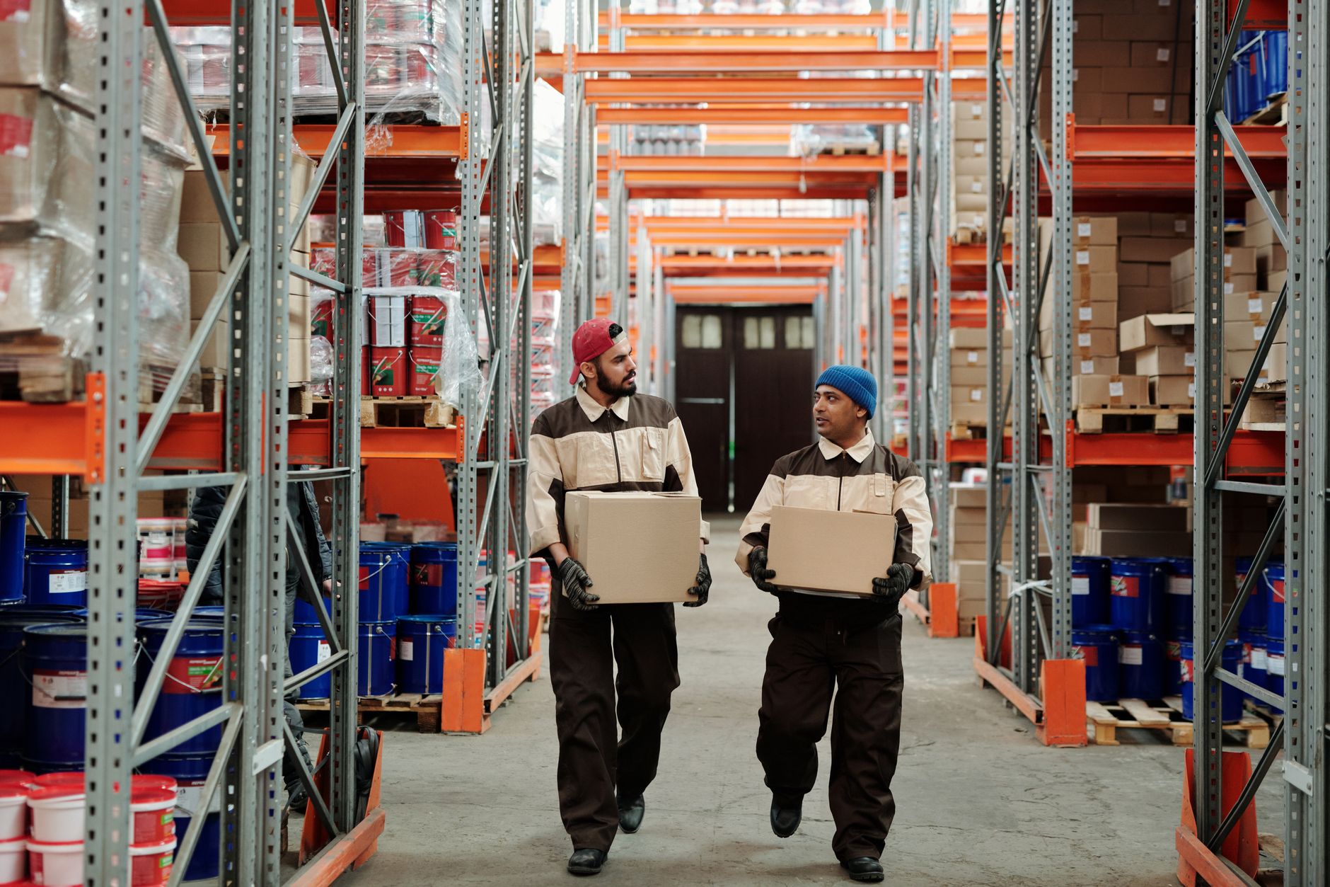 Two workers carrying boxes in a warehouse aisle, engaged in