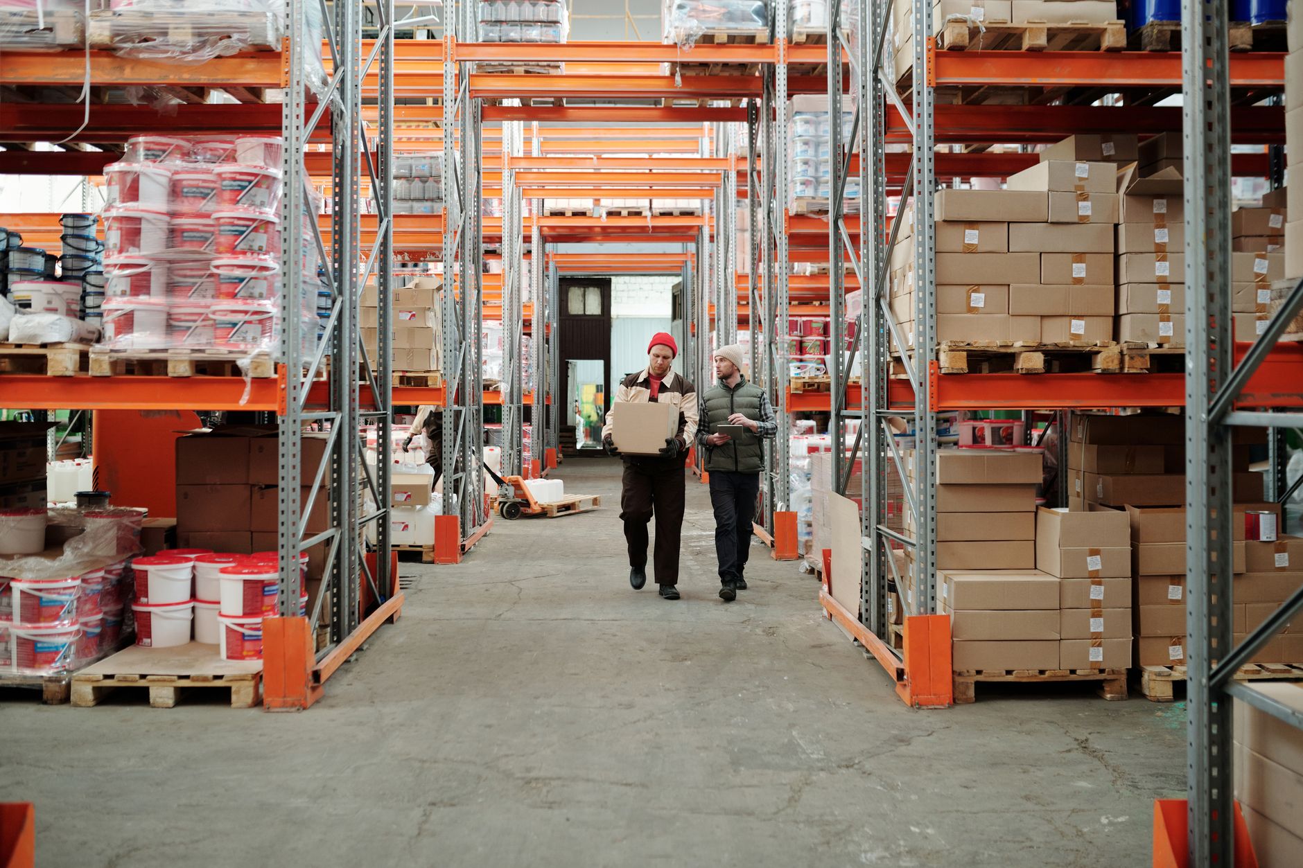 Two workers handle a package in a spacious warehouse surroun