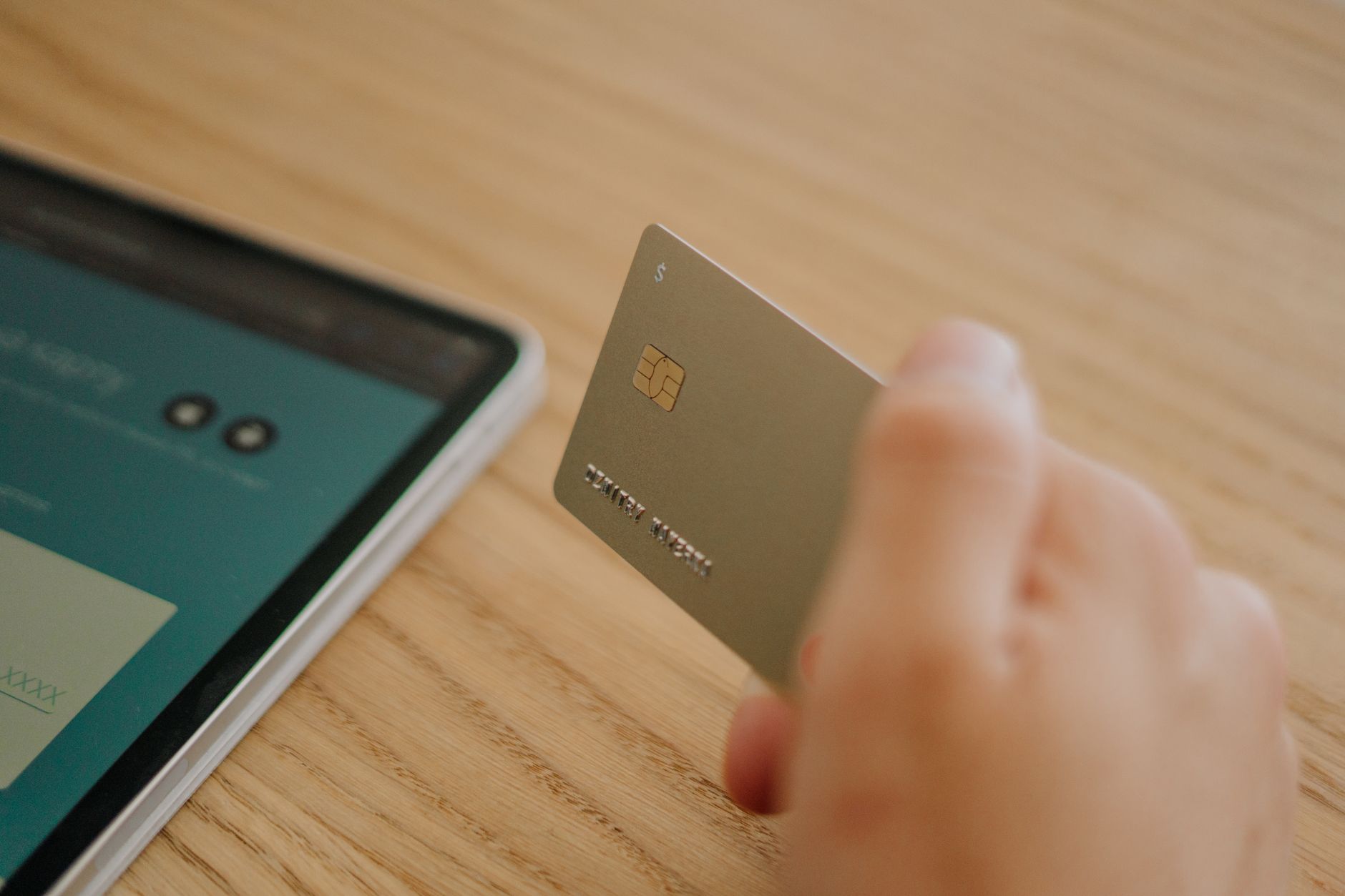 Close-up of a hand holding a credit card near a tablet, depi