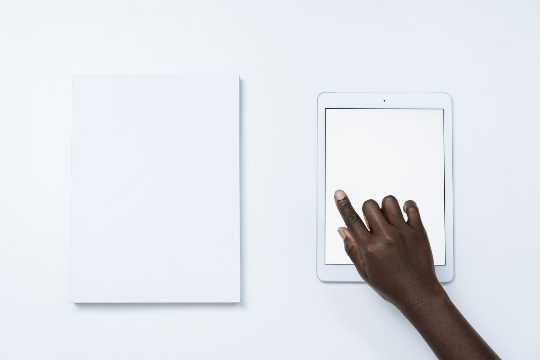 A hand interacting with a tablet next to blank paper on a wh