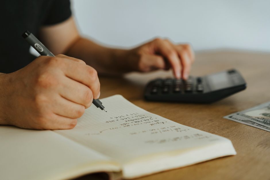 Close-up of hands writing calculations in a notebook with a