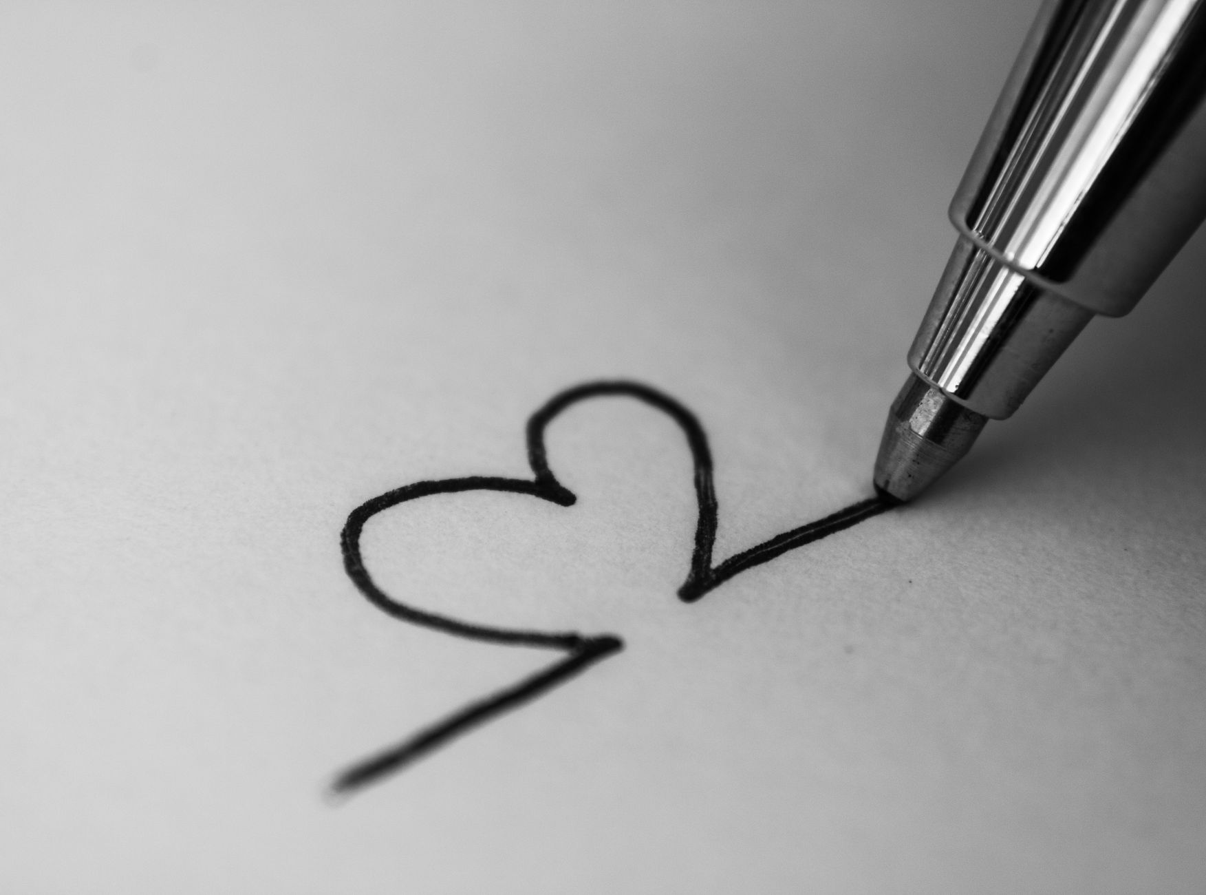 A monochrome close-up of a pen drawing a heart on paper, sym