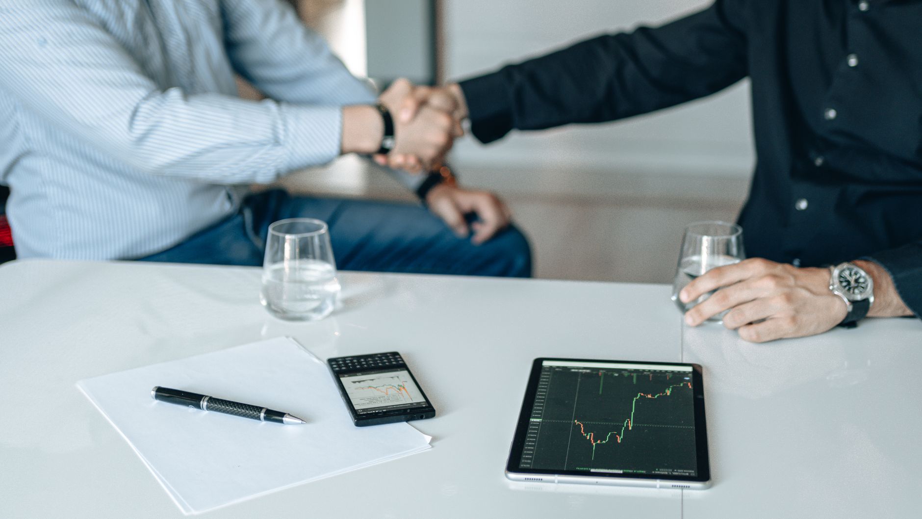 Business meeting with handshake and financial analysis displ