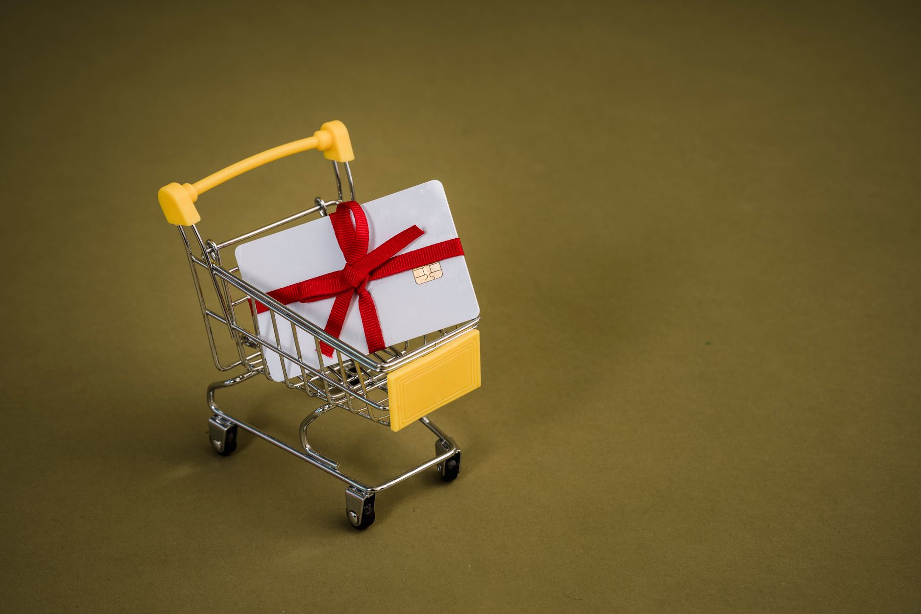 A gift card with a red bow sits in a mini shopping cart on a