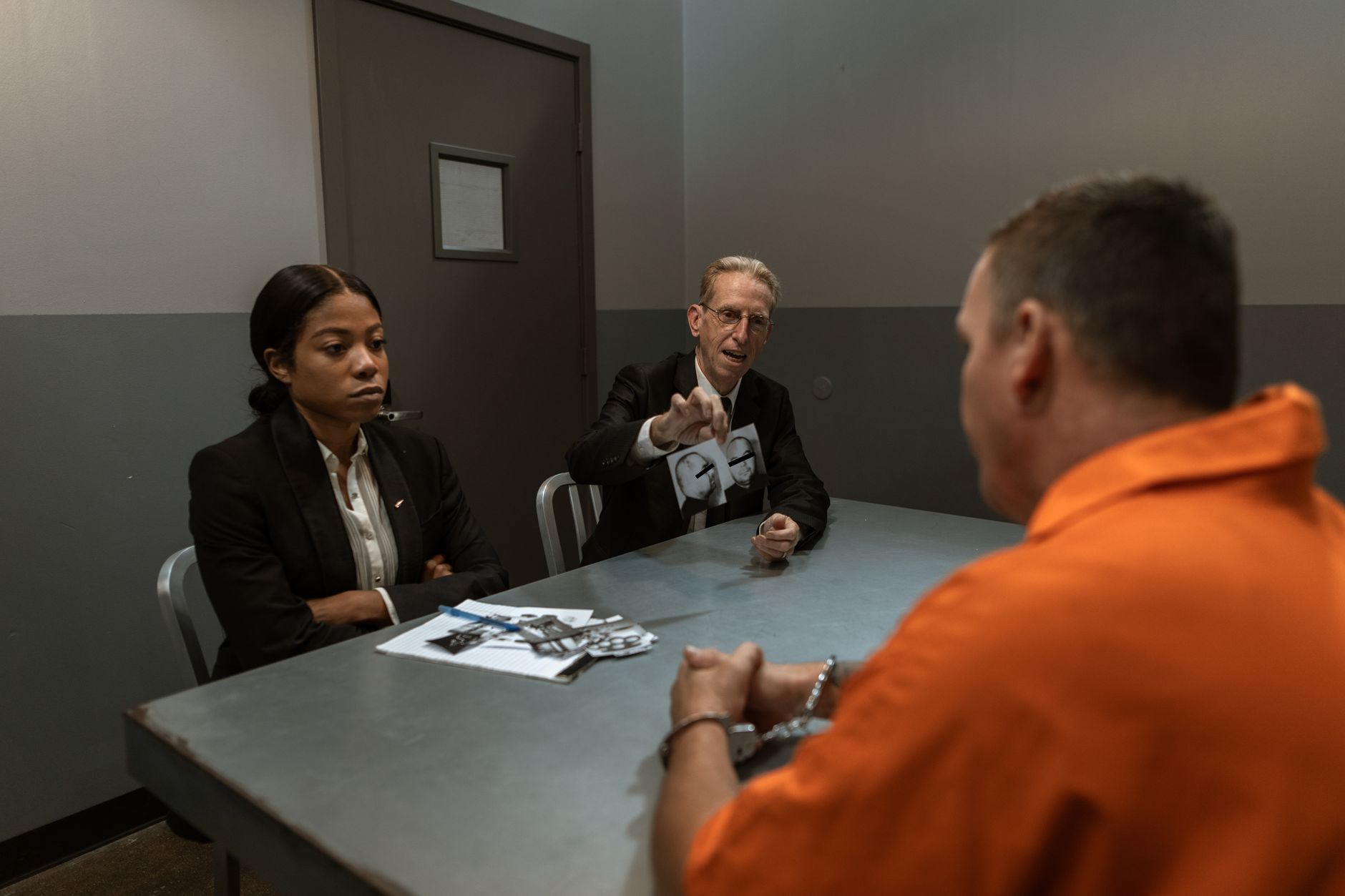 A suspect in an orange jumpsuit is interrogated by detective
