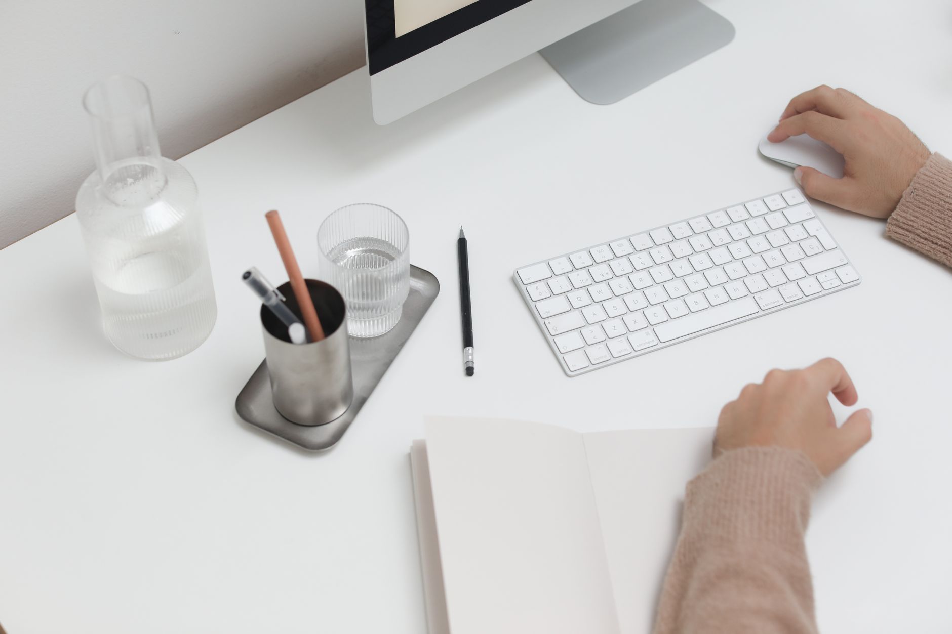 High angle of crop anonymous person sitting at table with wireless computer and office supplies while working online