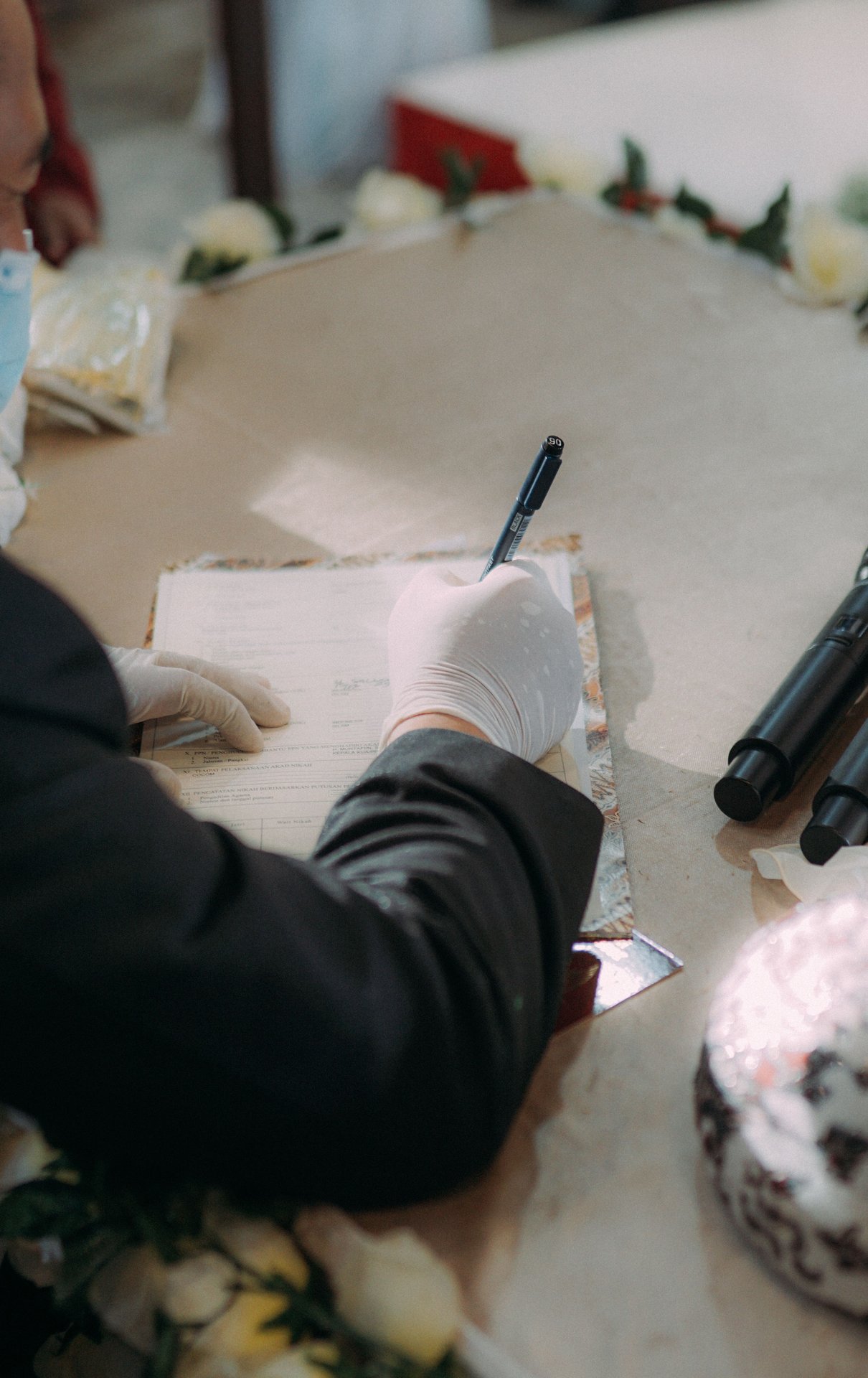 A person wearing gloves writes on paper at a decorated table, suggesting safety.