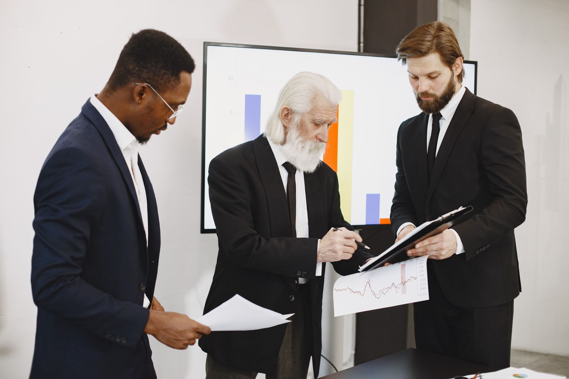 Three businessmen in suits reviewing reports and graphs duri