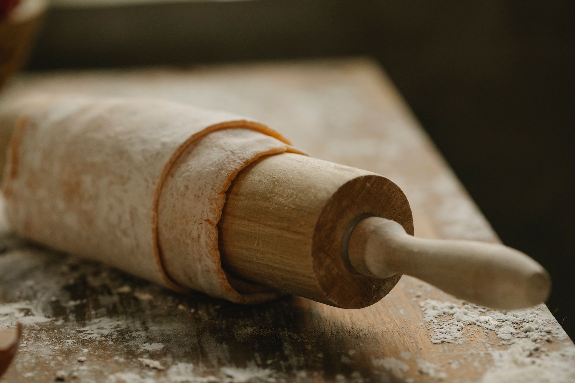 Rolling pin with soft thin dough on wooden table with spille