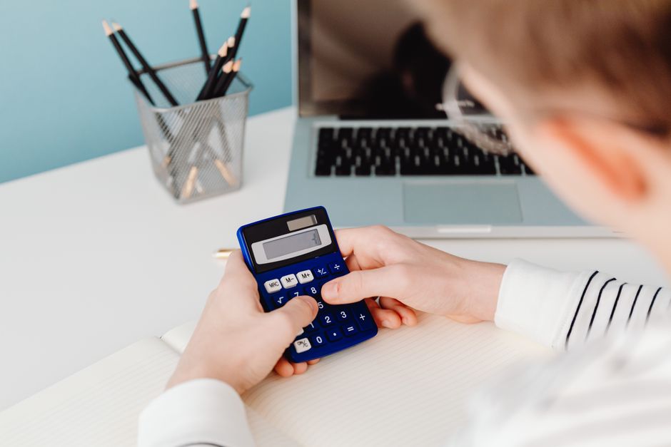 Close-up of hands using a blue calculator at a desk with a l