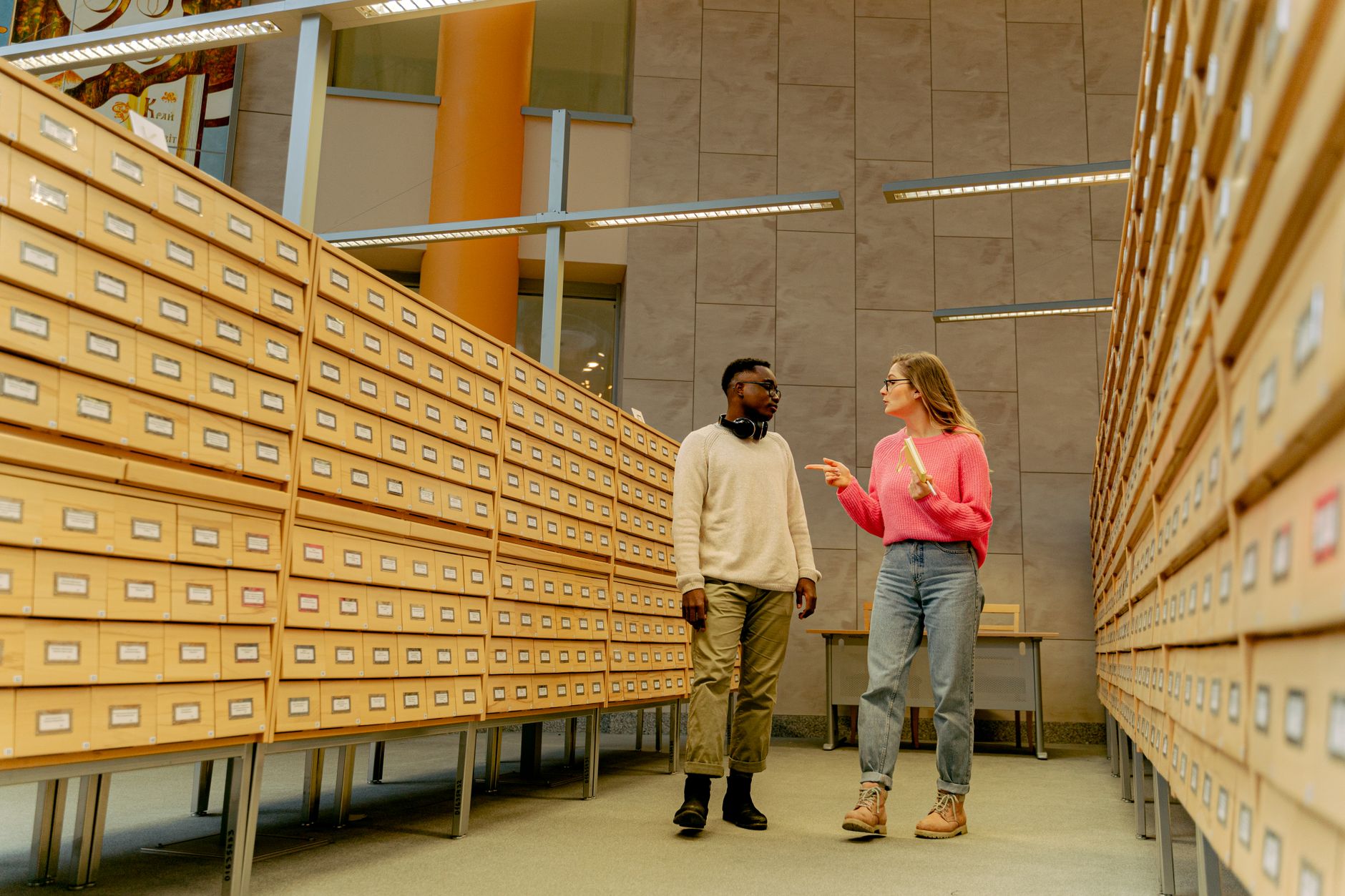 Two adults conversing in a library archive aisle surrounded