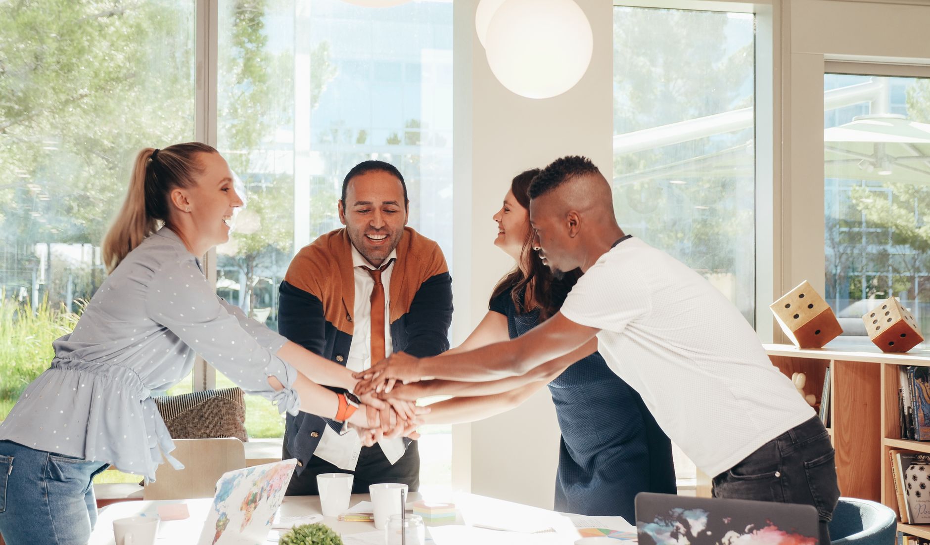 Content multiethnic colleagues joining hands above table wit
